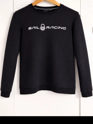 Svart Sail Racing hoodie - Svart hoodie från Sail Racing med vit logotyptryck på bröstet. Klassisk rund halsringning och ribbade muddar vid ärmslut och nederkant. Endast 200kr. Storlek: 170 (XS funksr också) Hör av dej vid intresse 😁