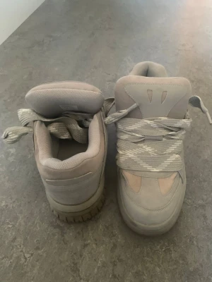 Bershka sneakers  - Snygga chunky sneakers i ljusgrått med breda, mönstrade snören och vadderad plös. Skorna har en robust sula och detaljer i både mocka och textil. Perfekta för dig som gillar streetwear och vill sticka ut med dina skor.