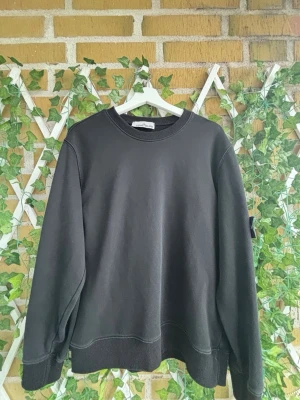 Svart sweatshirt från Stone Island - Säljer en svart sweatshirt från Stone Island med klassisk rund halsringning och ribbade muddar. Tröjan har den ikoniska Stone Island-loggan på vänster ärm. Perfekt för en stilren och avslappnad look.  46cm på bredden och 62cm på längden  