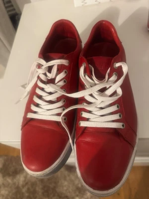 Röda sneakers med vita snören - Sulan är svart, inte vit, den här skomodellen är inte smutsig...Stilrena röda sneakers med vita snören och vit sula. Skorna har en klassisk låg modell och är tillverkade i slätt material som ger en clean look. Perfekta för dig som vill sticka ut med färg på fötterna. Passar till både jeans och shorts.