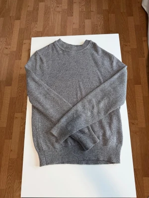 Grå stickad tröja HM - En stilren grå stickad tröja med rund halsringning och långa ärmar. Tröjan har ribbstickade muddar vid ärmslut och nederkant. Perfekt för lager-på-lager och enkel att matcha med olika outfits.