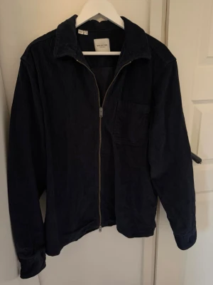 Svart manchesterovershirt - Svart overshirt från Selected med dragkedja framtill och bröstficka. Tillverkad i mjuk manchester som ger en skön och avslappnad look. Klassisk krage och långa ärmar, perfekt nu till våren!