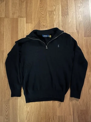 Ralph Laurent halfzip - Svart tröja med halvzip och klassisk Polo Ralph Lauren-logga på bröstet. Tröjan har ribbade muddar och krage, perfekt för en stilren look. Materialet är mjukt och bekvämt, och modellen är långärmad med en något lös passform.