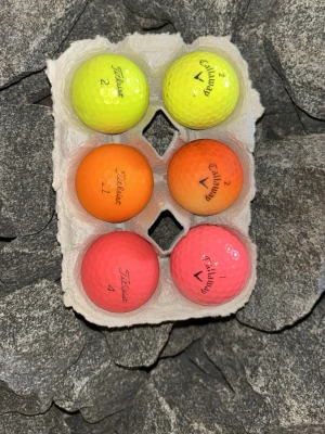 Färgglada golfbollar Titleist & Callaway - Sex golfbollar i olika färger från Titleist en prov1 och Callaway. Två gula, två orange och två rosa bollar, alla med tydliga loggor och siffror. Perfekt för dig som vill sticka ut på golfbanan med färgglada bollar i slitstarkt material.