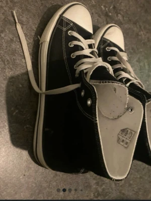 Svarta höga sneakers med vita detaljer - Klassiska svarta sneakers med högt skaft och vita snören. Skorna har vit tå, vit sula och tydliga kontrastsömmar. Ovandelen är i canvas och sulan i gummi. Perfekta för en avslappnad streetstil.