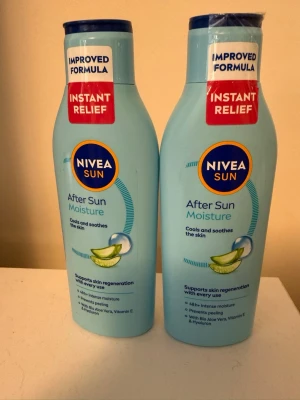 Nivea Sun After Sun Moisture duo - Två ljusblå flaskor Nivea Sun After Sun Moisture med förbättrad formula. Innehåller aloe vera och vitamin E för att återfukta och lugna huden efter solning. Flaskorna har blått lock och röd etikett med texten 'Instant Relief'.