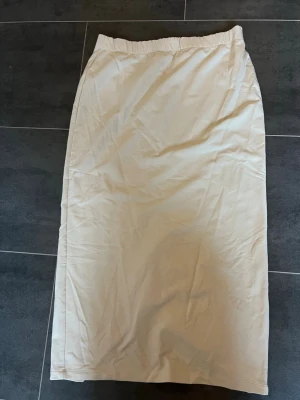 Beige långkjol med slits från Aimn - Stilren beige långkjol från Aimn med elastisk midja och diskret slits baktill. Kjolen har en rak passform och är tillverkad i ett mjukt bomullsmaterial. Perfekt för en clean och avslappnad look.