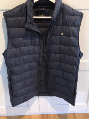 Mörkblå dunväst Morris - Stilren mörkblå dunväst från Morris med quiltad design.. Västen har dragkedja framtill och en liten logga på bröstet. Perfekt för lager-på-lager och håller dig varm under kyliga dagar.