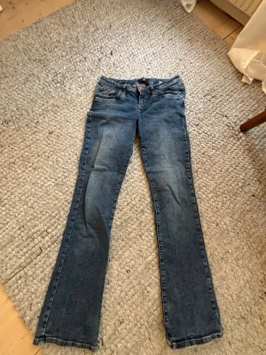 Blå bootcut jeans från LTB - Snygga blå bootcut jeans från LTB med klassisk femficksdesign och slitningar på låren. Jeansen har låg midja och kopparfärgade nitar.