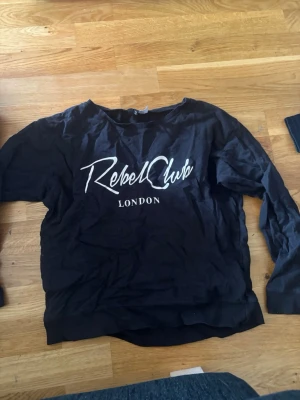 Svart sweatshirt - Svart sweatshirt med vit text 'Rebel Club London' på bröstet. Strl M