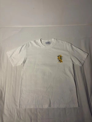 Vit Casa Blanca t-shirt med citrontryck - Säljer en vit t-shirt från Casa Blanca med färgglatt citrontryck på bröstet och stort motiv med gula citroner och gröna blad på ryggen. T-shirten har rund hals och korta ärmar. Perfekt för dig som gillar fräscha prints och stilren design.