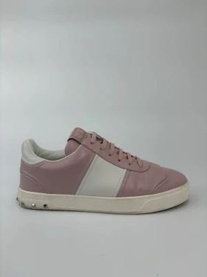 Valentino flycrew skor - Snygga sneakers i rosa och vitt läder från Valentino. Skorna har klassisk låg modell, vita detaljer och coola nitar på hälen. Perfekta för dig som vill ha en stilren men ändå unik look. Tjock vit sula och matchande rosa skosnören.