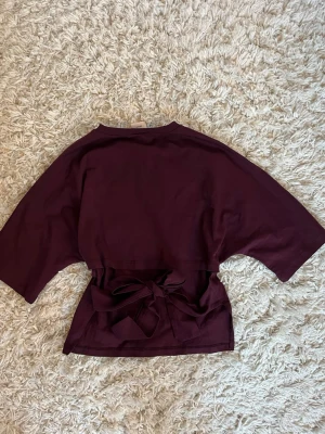 Vinröd topp med knyt i ryggen - Snygg vinröd topp med korta ärmar och bred knytning i midjan som ger en cool och trendig look. Andvänd väldigt få gånger så den är nästan som ny❤️säljs inte längre i denna fina färg!❤️