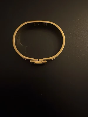 Hermès Clic H armband guld och vitt - Säljer ett Hermès Clic H armband i guldpläterad metall med vita emaljdetaljer. Armbandet har den ikoniska H-formade låset framtill och en stilren, rundad form. Perfekt accessoar för att lyfta din outfit.