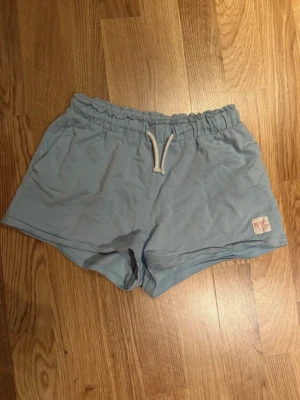Ljusblå shorts med snörning NYC - Snygga ljusblå shorts från NYC med elastisk midja och vit snörning framtill. Mjukt bomullsmaterial och avslappnad passform. Liten patch med NYC-logga på ena benet. Perfekta för varma dagar eller chill hemma.💗