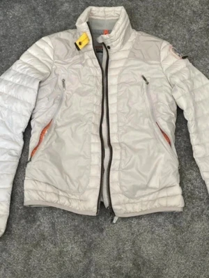 Parajumpers jacka  - Snygg ljus pufferjacka från Parajumpers med hög krage och dragkedja framtill. Jackan har två snedställda fickor med dragkedja, quiltad design och coola detaljer som gul rem vid halsen och orange insida. Perfekt för kalla dagar och riktigt trendig look.