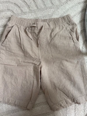 Beiga linneshorts från Kappahl - Snygga beiga linnebyxor från Kappahl i storlek 164. Byxorna har resår och dragsko i midjan samt två sidofickor. Tillverkade i ett luftigt linnematerial som passar perfekt för varma dagar.