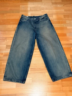 Vida svarta jeans med rak passform - Säljer ett par svarta jeans med breda ben och rak passform. Jeansen har klassisk femficksdesign och är tillverkade i denim. Perfekta för en avslappnad och trendig stil. 34/32