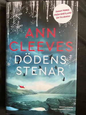 Dödens stenar av Ann Cleeves - Spännande kriminalroman av Ann Cleeves, känd för sina brittiska deckare. Omslaget är mörkt med snöflingor, is och en dramatisk kustmiljö. Boken är inbunden och har en mystisk, vintrig känsla. Perfekt för dig som gillar spänning och starka karaktärer.