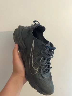 Nike React Element 55 svarta sneakers - Nike React Element 55 sneakers i svart med vit Swoosh-logga på sidan. Skorna har en sportig design med perforerat meshmaterial för bra andningsförmåga och en chunky sula med React-dämpning. Klassisk snörning och låg profil för en clean look.