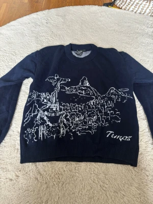 Temps brazil - Mörkblå stickad tröja från Temps med vit brodyr av stadsmotiv och texten 'Temps' framtill. Rund halsringning och ribbade muddar vid ärmslut och nederkant. Perfekt för dig som gillar unika detaljer.