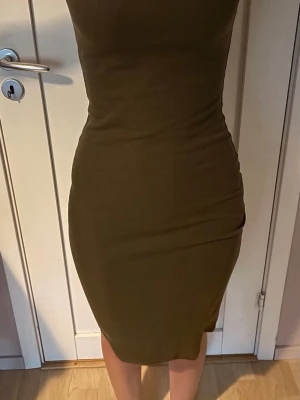 Olivgrön ribbad klänning - Tajt olivgrön klänning i ribbad bomull med kroppsnära passform och ärmlös design. Perfekt för dig som gillar en enkel men stilren look. Klänningen har en kort längd och markerar midjan snyggt.