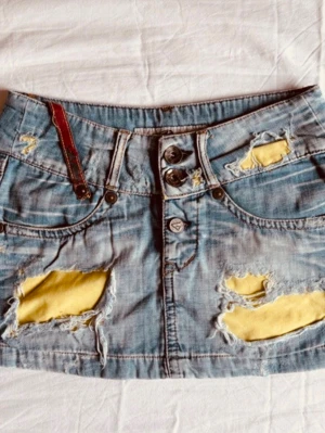 Jeanskjol med slitningar från Miss Greenage - Måtten är 34 rakt över pris kan diskuteras Cool ljusblå jeanskjol från Miss Greenage med slitna detaljer och gula lappar under de trasiga partierna. Kjolen har knappar framtill och klassiska fickor. Perfekt för dig som gillar en edgy och trendig stil.