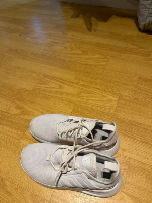 Vita Adidas sneakers med mesh - Snygga vita sneakers från Adidas med lågt skaft och klassisk design. Skorna har ovandel i mesh och syntetmaterial, samt snörning framtill. Perfekta för en clean och sportig look. Diskreta ränder på sidan och bekväm innersula.