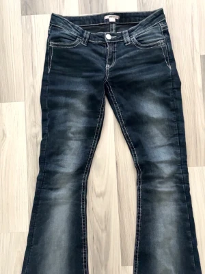 mörkblå bootcut jeans från Gina 14+ - Mörkblå bootcut jeans med snygga slitningar och kontrastsömmar. Bakfickorna har stora broderade mönster i vitt och grått som ger en unik look. Klassisk femficksmodell med knapp och dragkedja. Perfekta för dig som gillar detaljer och en cool stil. Lite slitna längst ner pga att dem var lite för långa för mig och därmed blivit lite nertrampade men inget man tänker på💗🩷