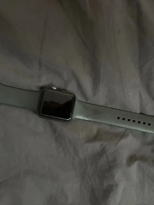 Apple Watch svart aluminium - Snygg Apple Watch med svart aluminiumboett och svart silikonarmband. Klockan har en fyrkantig touchskärm och pulssensor på baksidan. Perfekt för dig som vill ha koll på träning, notiser och hälsa direkt på handleden.