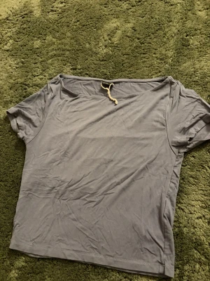 Grå t-shirt croppad - En enkel grå t-shirt med korta ärmar och en snygg snörningsdetalj vid halsringningen. T-shirten har en rak passform och är tillverkad i ett mjukt material som känns skönt mot huden. Perfekt för en avslappnad stil.