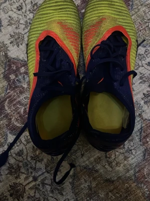 Nike Phantom GT2 färgglada fotbollsskor - Säljer ett par Nike Phantom GT2 fotbollsskor elite  i blått, gult och rött . Skorna har snörning, dobbar för bra grepp på planen och är tillverkade i syntetmaterial för lätt känsla och bra bollkontroll.