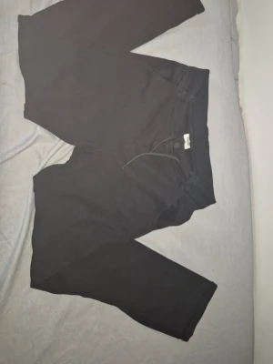 Svarta mjukisbyxor med dragsko - Svarta mjukisbyxor med dragsko i midjan och raka ben. Byxorna har två bakfickor och är tillverkade i ett mjukt och bekvämt material, perfekt för en avslappnad stil. Passar dig som gillar enkel och stilren design.