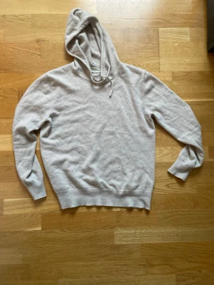 Beige cashmere hoodie från Sayles - Mysig beige/khaki färgad hoodie från Sayless i mjuk cashmere. Klassisk modell med huva och dragsko, ribbade muddar vid ärmslut och nederkant. Perfekt för en chill och stilren look.