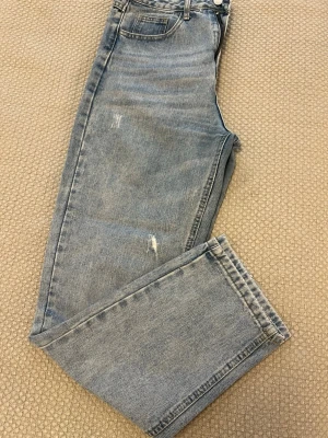 Ljusblå raka jeans - Snygga ljusblå jeans med raka ben och diskreta slitningar på låret och knät. Klassisk femficksmodell med knapp och dragkedja. Jeansen har en avslappnad passform och är tillverkade i bomullsdenim. 