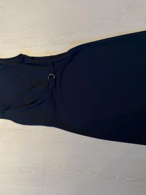 Marinblå långklänning från H&M - Snygg marinblå långklänning från H&M med markerad midja och dekorativt bälte med metallspänne. Klänningen har en elegant och enkel design som passar perfekt till speciella tillfällen. Tillverkad i ett mjukt och följsamt material.
