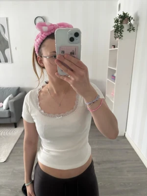 Vit croppad topp med spetskant - Söt vit croppad topp med korta ärmar och dekorativ spetskant runt halsen. Perfekt för att skapa en fräsch och trendig look. Toppens material känns mjukt och bekvämt mot huden.