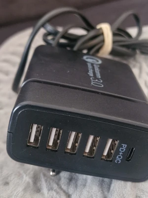 Svart USB-laddare med 6 portar - Multiladdare i svart plast med fem USB-A portar och en USB-C port märkt PD+QC. Perfekt för att ladda flera enheter samtidigt, t.ex. mobil, surfplatta och hörlurar. Kompakt design med fast strömkabel. Stöd för snabbladdning via Quick Charge 3.0.