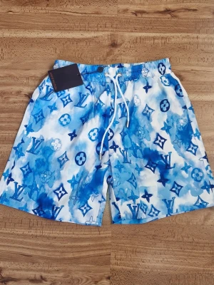 Blå Louis Vuitton shorts - Snygga blå och vita badshorts från Louis Vuitton med ikoniskt monogrammönster och snörning i midjan. Shortsen har elastisk midja och bakficka, perfekta för sommaren och strandhäng.
