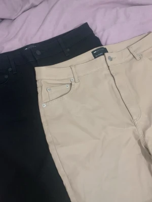 Beiga och svarta jeans från Selected - Två par jeans från Asos, ett par i beige och ett par i svart. Klassisk femficksmodell med bälteshällor och knappgylf. Snygg passform och stilren design, perfekta till många olika looks. Materialet känns mjukt och följsamt.