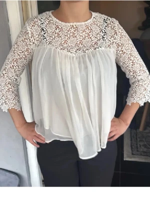 Vit Zara blus med spetsdetaljer - Söt vit blus med transparent spets upptill och på ärmarna. Blusen har en lös passform och trekvartsärmar i spets, medan nederdelen är i ett tunt, flowy tyg. Perfekt för dig som gillar romantisk och bohemisk stil.