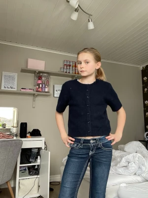 Mörkblå jeans med vita sömmar - Snygga mörkblå jeans med kontrasterande vita sömmar och dekorativa fickor bak med knappar. Jeansen har låg midja och raka ben, vilket ger en cool och ungdomlig look. Perfekta för dig som vill ha ett par jeans som sticker ut lite extra.
