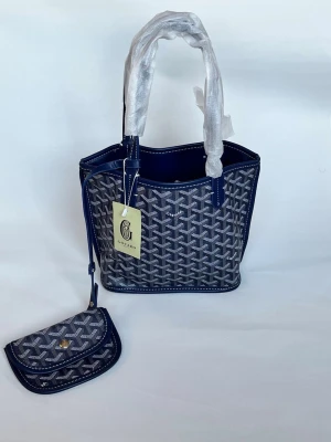 Blå Goyard handväska med mönster - Snygg blå handväska från Goyard med klassiskt grafiskt mönster och matchande liten plånbok. Väskan har två handtag och detaljer i mörkblått läder. Perfekt för dig som vill ha en trendig och unik accessoar.