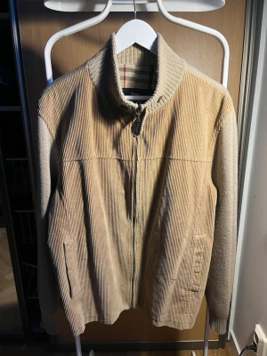 Beige manchesterjacka från Burberry - Säljer en beige manchesterjacka från Burberry med klassiskt rutigt foder. Jackan har ribbad krage och muddar, dragkedja framtill och två fickor. Perfekt för dig som gillar stilrena och tidlösa plagg. Passar M lite loose fit då 