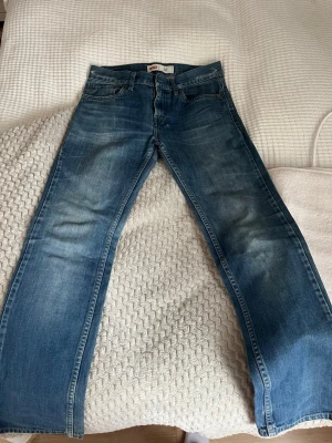 Levi's 511 Slim blå jeans - Säljer ett par klassiska Levi's 511 Slim jeans i blå denim med snygga slitningar och femficksdesign. Jeansen har en smal passform och är tillverkade i bomull. Perfekt för dig som gillar en tidlös och cool look.