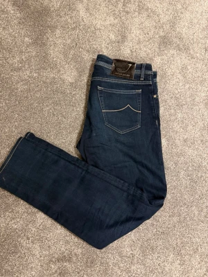 Mörkblå jeans från Jacob Cohen - Snygga mörkblå jeans från Jacob Cohen med klassisk femficksmodell och kontrastsömmar på bakfickan. Jeansen har en patch med logga bak i midjan och är tillverkade i mjukt denimtyg som ger en skön passform.