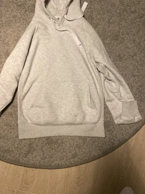 Ljusgrå hoodie  - Snygg ljusgrå hoodie i mjukt bomullsmaterial. Klassisk modell med huva och dragsko, samt en stor magficka framtill. Ribbstickade muddar vid ärmslut och nederkant ger en clean look. Perfekt för chill dagar eller när du vill vara bekväm.