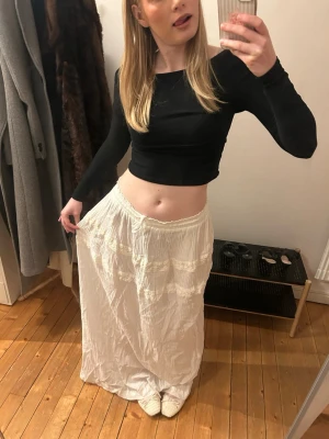 Vit långkjol med spetsdetaljer - Säljer en flowy vit långkjol med fina spetsdetaljer. INTE STRYKT. Kjolen har en romantisk vibe och är perfekt för varma dagar. Materialet känns luftigt och bekvämt, och kjolen har en elastisk midja för skön passform. Passar storlekar S-L beroende på önskad passform. Lätt att justera 