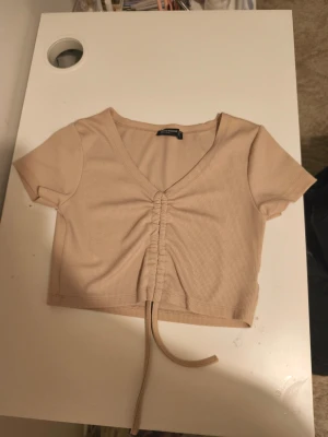 Beige croppad ribbad topp med snörning - Trendig beige croppad topp från Kechi woman med ribbad struktur och snörning framtill. Toppen har v-ringning och korta ärmar, perfekt för en avslappnad och snygg look. Passformen är slim och materialet känns mjukt mot huden.
