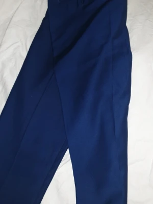 Mörkblå kostymbyxor i klassisk modell - Snygga mörkblå kostymbyxor med raka ben och pressveck. Byxorna har en klassisk passform och stängs med knapp och dragkedja. Perfekta till både skjorta och t-shirt för en clean look.